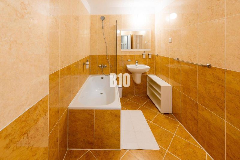 A bathroom in a studio apartment with light tiles, a bathtub, and a sink.