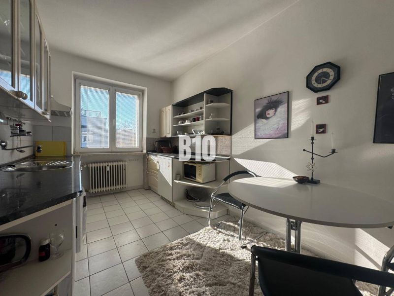 Kitchen in a 2-room apartment with white cabinets, a window, and a dining table.