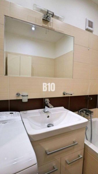 A bathroom in a 4-room apartment with a sink, mirror, and washing machine.