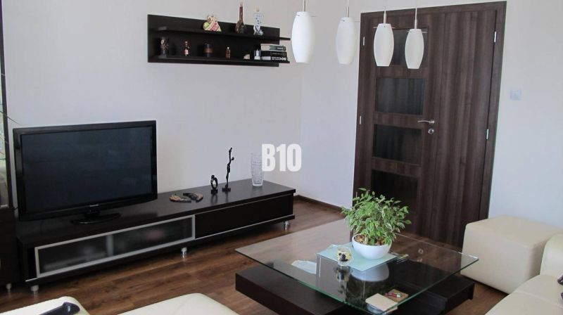 Living room with a television, shelves, a table, and a wooden decor floor in a 4-room apartment.