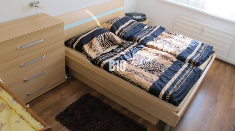 A bedroom with patterned bedding, a dresser, and a wooden decor floor in a 4-room apartment.