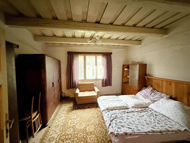 A bedroom in a family house with a wooden ceiling, a bed, and furniture.