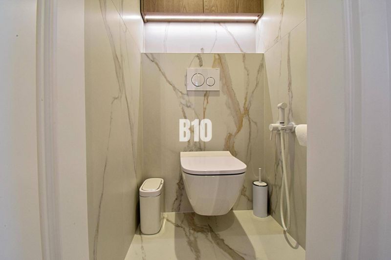 A toilet with marble tiles in a 3-room apartment, includes a wall-hung bowl and a bidet.