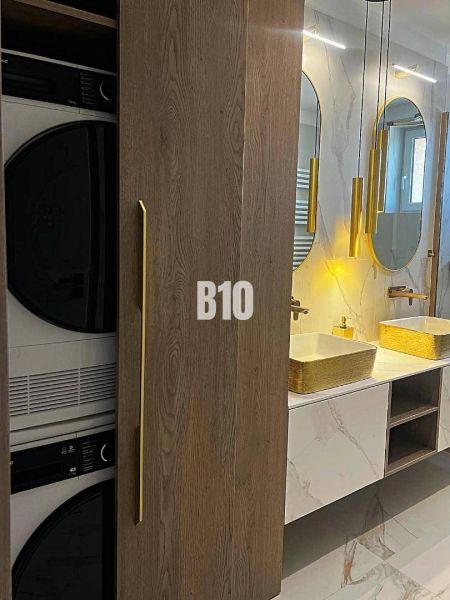 A bathroom with two sinks, a washing machine, and a dryer in a 3-room apartment, with a wooden decor floor.