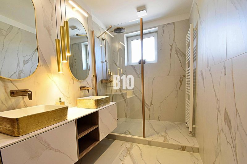 A bathroom in a 3-room apartment with marble tiles, two sinks, and a shower.