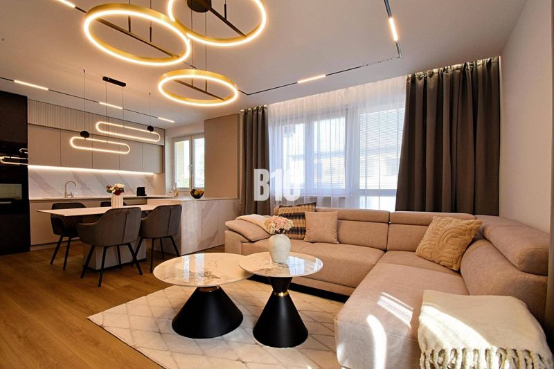 Living room with kitchen, wooden decor flooring, stylish lighting, and a comfortable sofa.