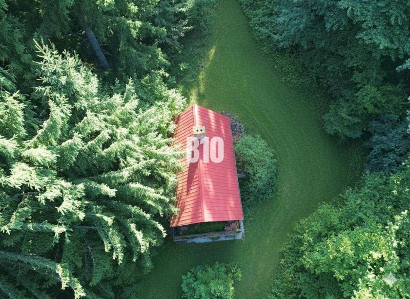 A cottage in Kunerad among the trees with a red roof and surrounding greenery.
