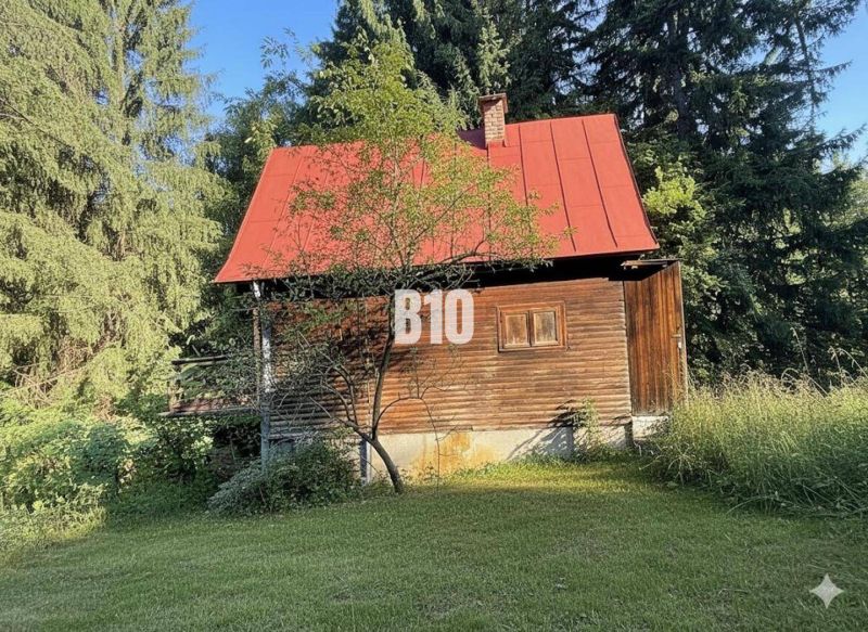 A wooden cottage in Kunerad with a red roof surrounded by forests and meadows.