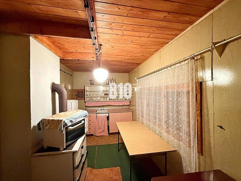 A kitchen in a cabin with a wooden ceiling and an antique stove, complemented by a curtain.