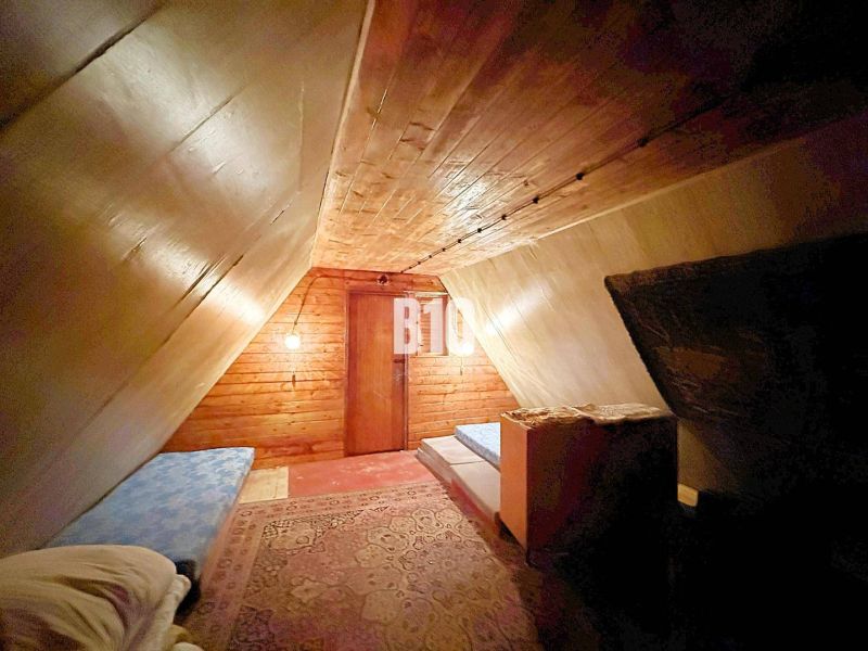 The attic of the cottage with a sloped ceiling, beds, and a wooden decor floor.