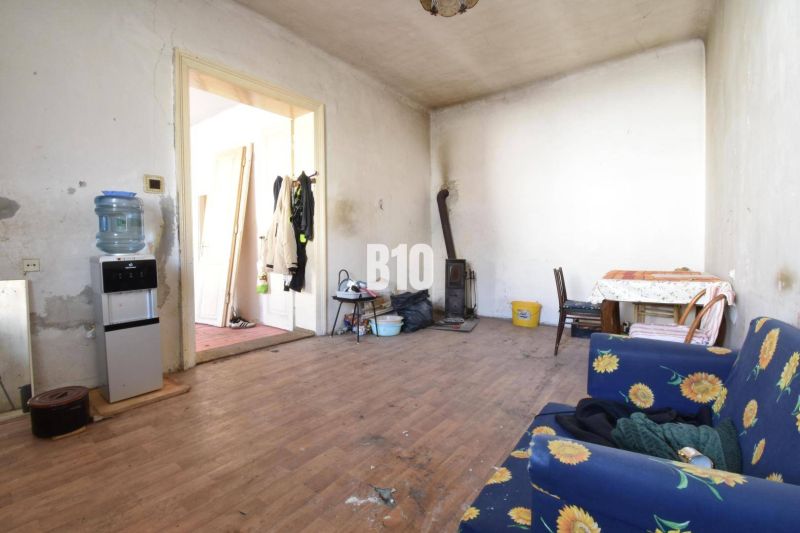 A room in a family house with a wooden decor floor, a stove, and furniture with floral fabric.