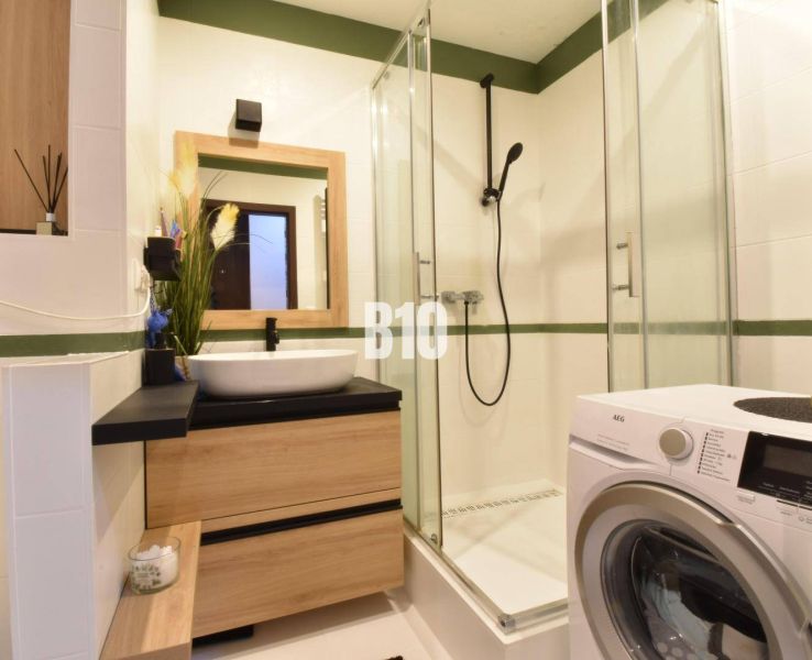 The bathroom in a three-room apartment includes a shower, a sink, and a washing machine.