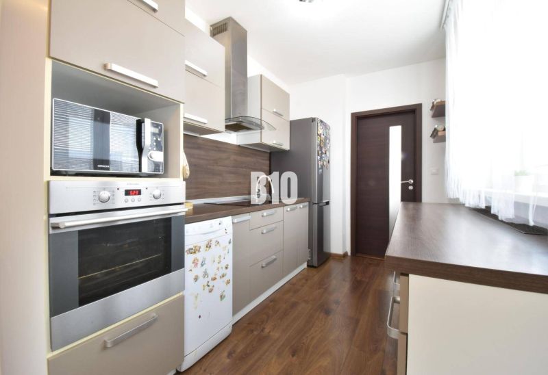 A kitchen in a 3-room apartment with a wooden decor floor and modern appliances.