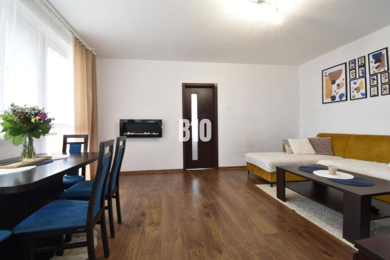 Living room in a three-room apartment with a wooden decor floor, sofa, and dining table.