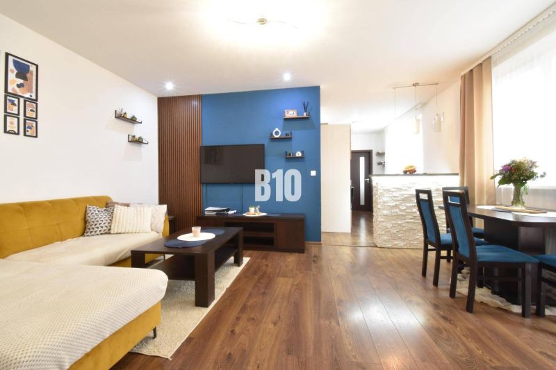 Living room with a sofa and a dining table in a 3-room apartment and a floor with a wooden decor.