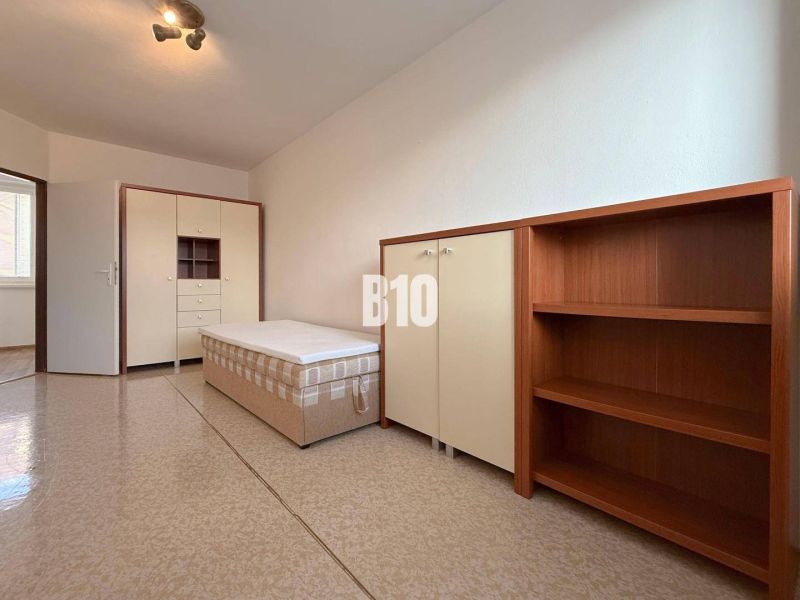 A bright room in a holiday apartment with a bed, wardrobe, and shelving unit.