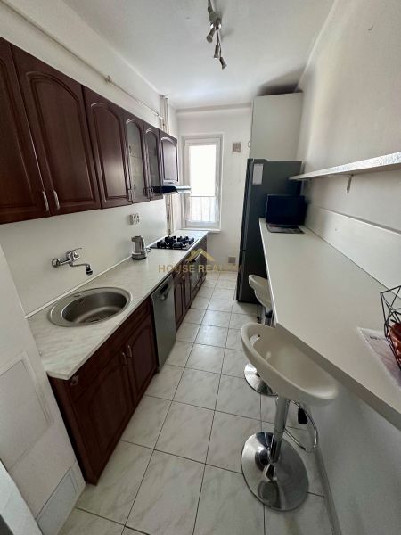 A narrow kitchen with a white countertop and wooden cabinets in a 3-room apartment.