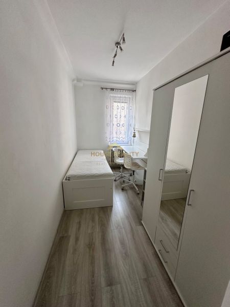 A simple room with a bed, a wardrobe, and a desk, with a wooden-patterned floor.