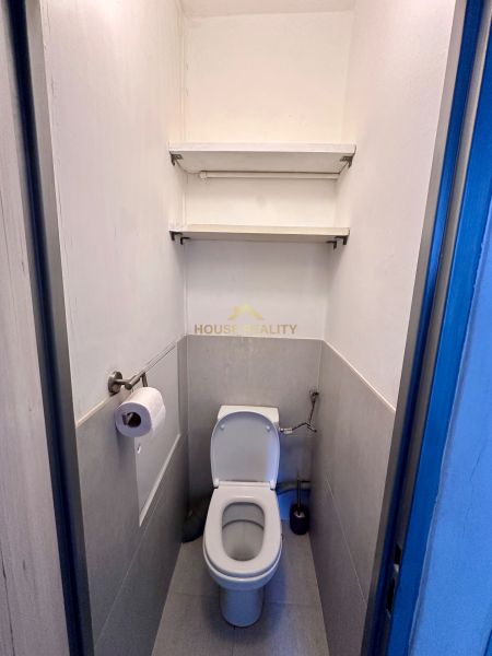 A bathroom in a 3-room apartment with two shelves on the wall.