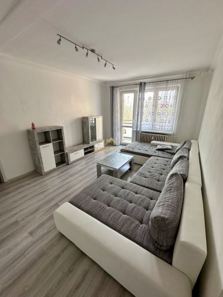 Living room in a 3-room apartment with a wooden decor floor, a large sofa, and a television.
