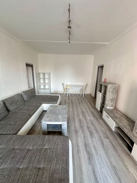 Living room with wood-patterned flooring and a gray sofa in a three-room apartment.