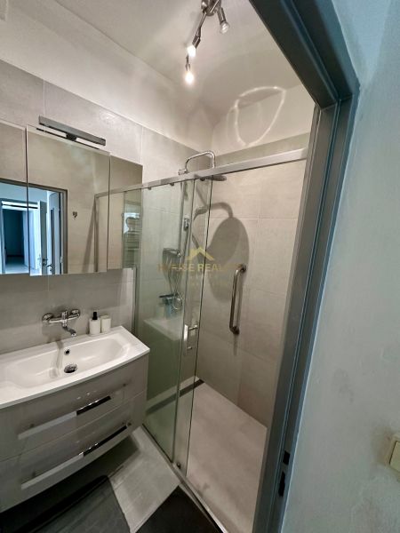 A bathroom in a 3-room apartment with a shower, a sink, and simple lighting.