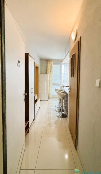 A narrow hallway in a one-room apartment with bar stools and a refrigerator.