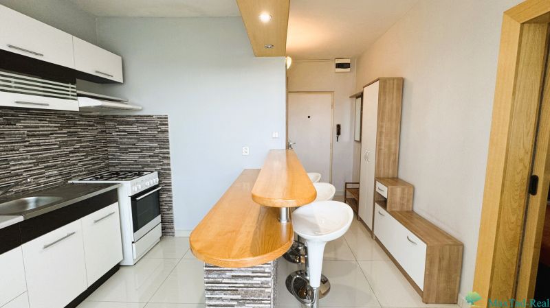 A kitchen with a bar counter and a tiled wall in a studio apartment.