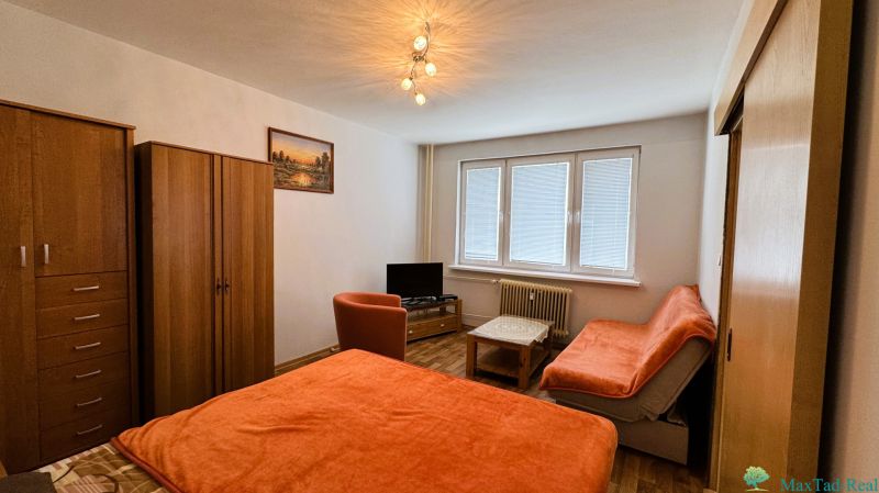 A room with furniture in a one-room apartment, a floor with a wooden decor, orange covers on the sofa.