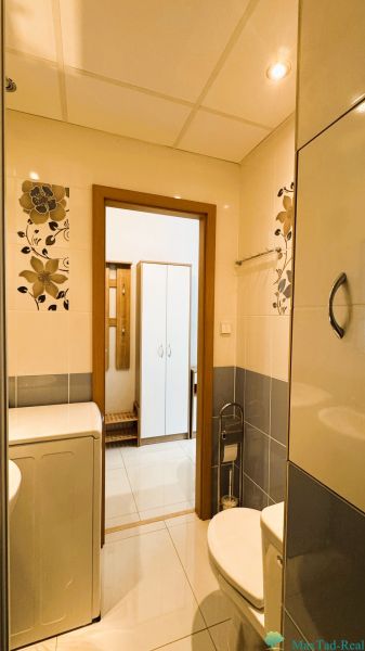 Bathroom in a one-room apartment with a washing machine, toilet, and floral decoration on the walls.