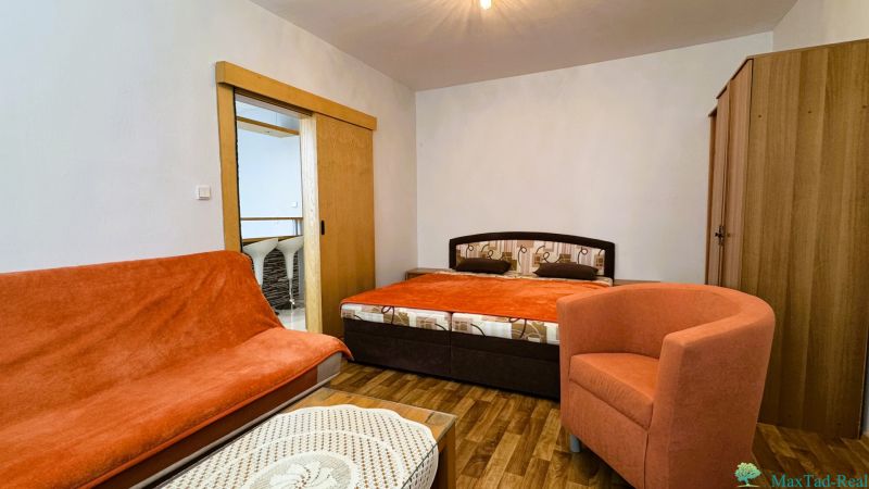 A room with a double bed, an orange armchair, and a wood-patterned floor.