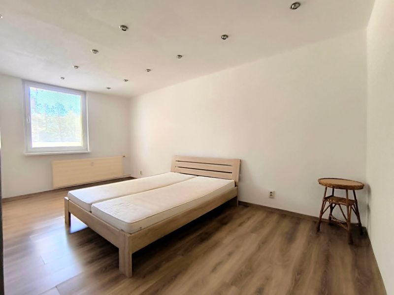 A bedroom with a light bed, chair, and wood-decorated floor in a studio apartment.