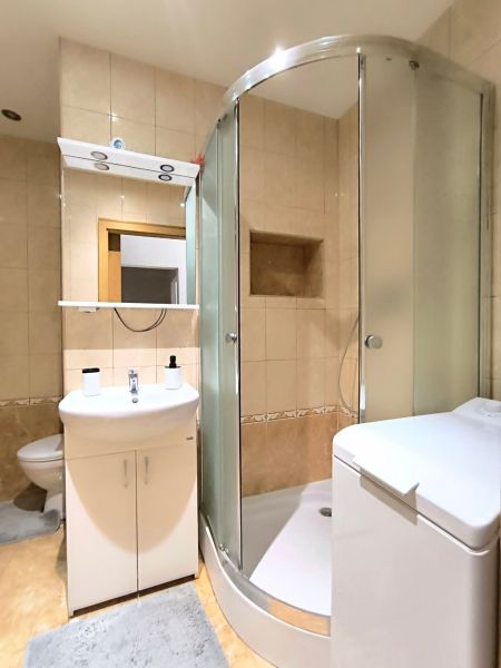 A bathroom with a corner shower and a washing machine in a studio apartment.