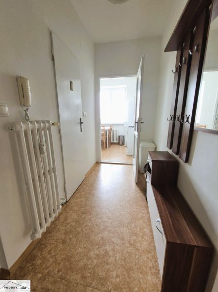 A hallway in a 3-room apartment with a wooden decor floor and an entrance to the kitchen.