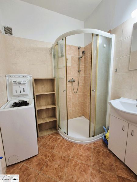 Bathroom in a 3-room apartment with a washing machine, shower corner, and cabinet under the sink.