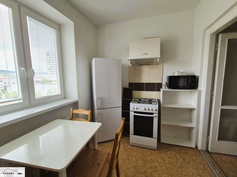 A kitchen of a 3-room apartment with a simple table, refrigerator, and stove.