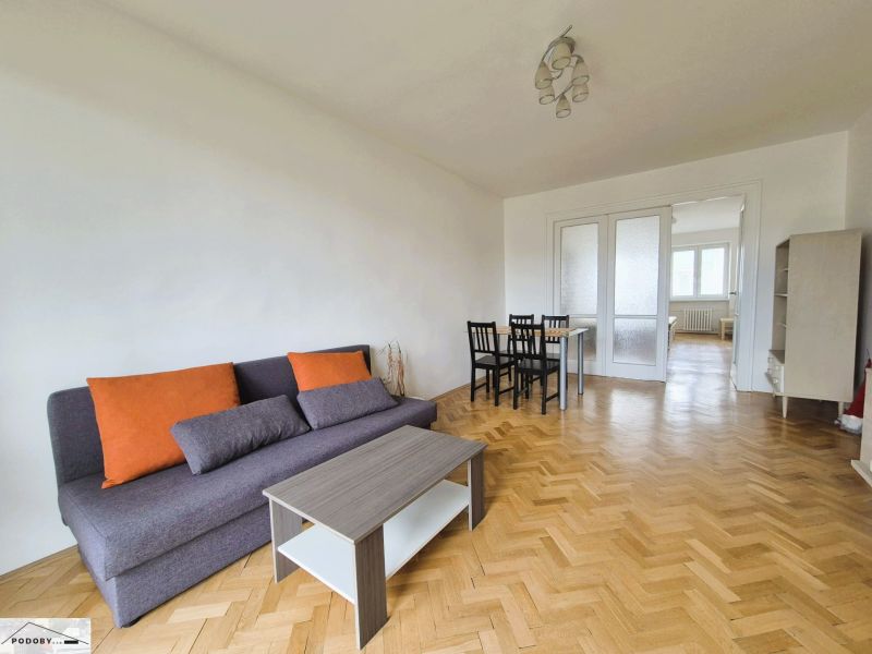 Living room with a sofa, table, and chairs in a 3-room apartment with a wooden decor floor.