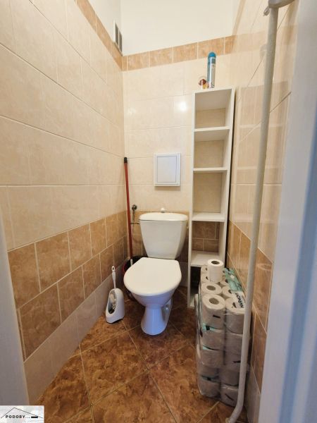 Bathroom with toilet, white tiles, and a shelf in a 3-room apartment.