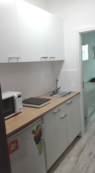 A kitchenette in a studio apartment with cabinets, a microwave, and a wooden decor floor.