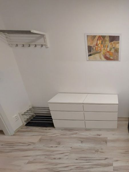 A studio apartment with a wood-patterned floor, white furniture, and a colorful painting on the wall.