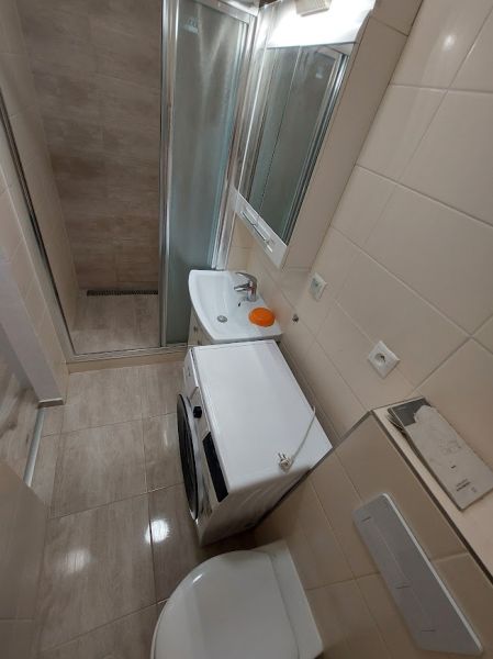 A bathroom in a studio apartment with a shower, washing machine, and sink in a compact space.