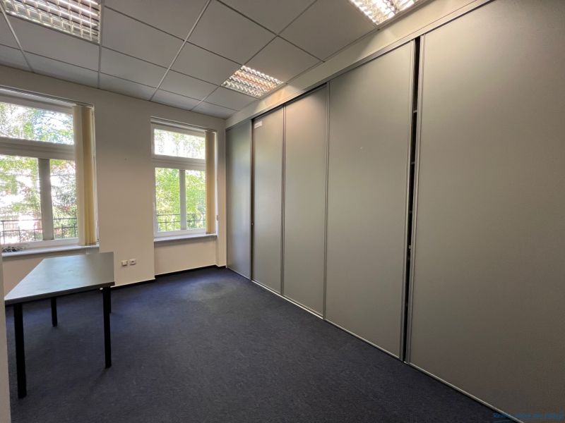 Offices with a large window and a closet, carpet, furniture in neutral colors.