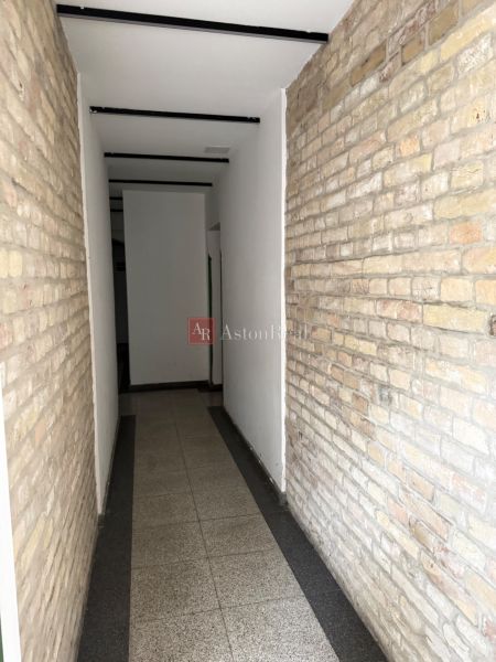 A narrow interior passage with a brick wall and light flooring in a two-room apartment.