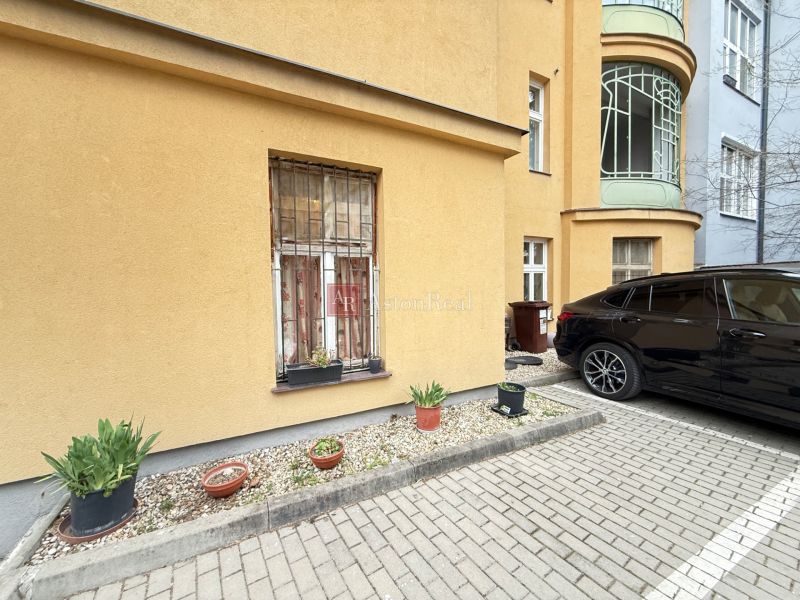 Parking in front of the building on Leškova Street in Bratislava with flower pots and a parked car.