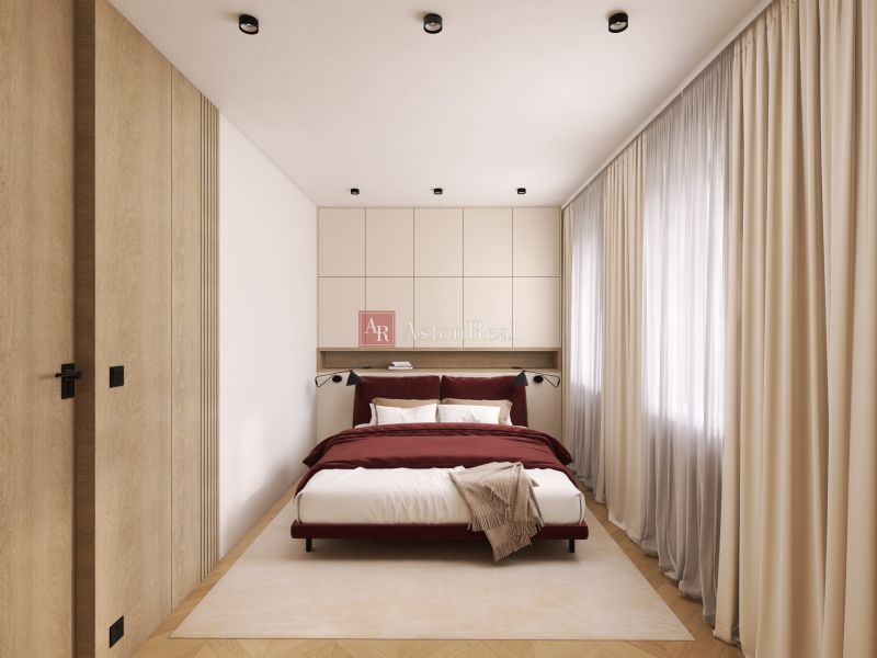 A bedroom in a two-room apartment with a wood-patterned floor and cream curtains.