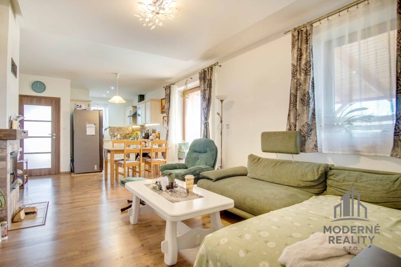 Living room of a family house with a kitchen, green sofa, wooden decor flooring.