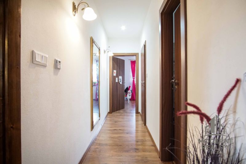 A hallway in a family house with a wooden decor floor and a mirror on the wall.