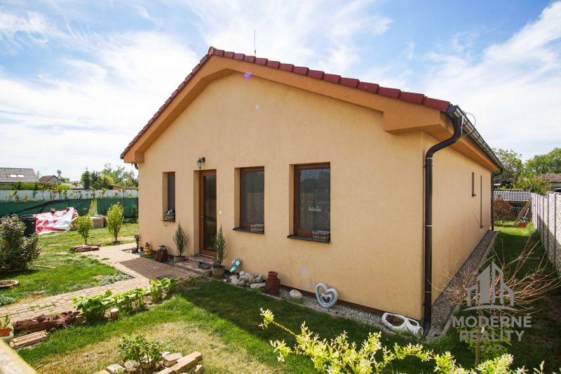 A family house in Andovce with a landscaped garden, yellow facade, and a sloped roof.