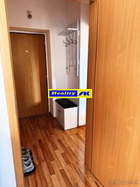 Hallway in a one-room apartment with a wooden decor floor and a coat rack.