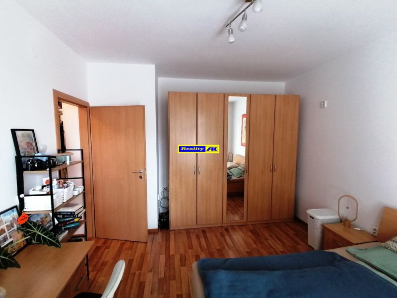 A bedroom in a one-room apartment with a wood-patterned floor, a wardrobe, and a desk.